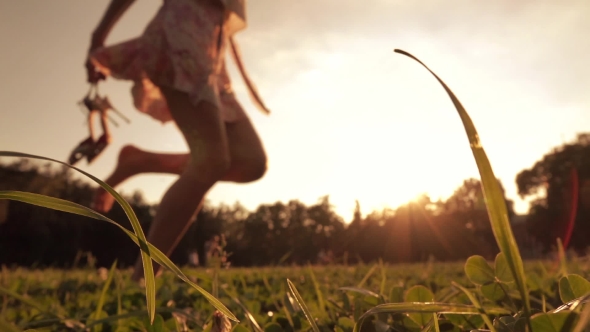 Girl Running Barefoot On The Grass Holding Her High Heels In Hand alt