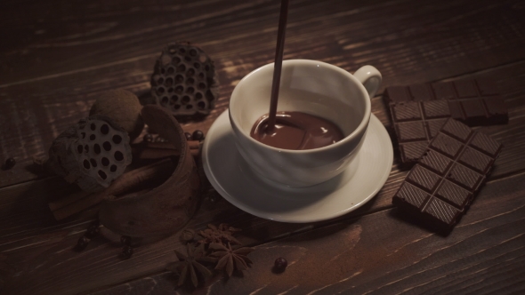 Pouring Hot Chocolate With Anise And Cinnamon Sticks On Dark Wooden Table
