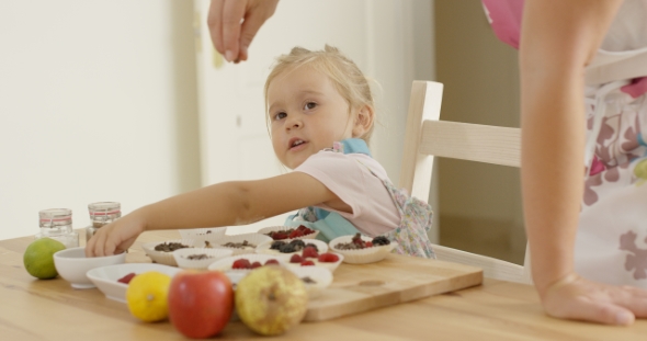 Child Watching Woman Sprinkle Candy On Muffins alt