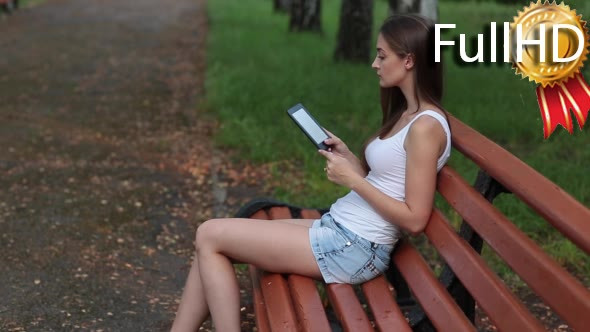 Woman Reading Ebook on a Park Bench