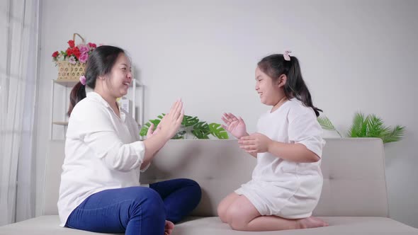 mom and kid sitting and playing hands game together with happy and laughing face on sofa alt