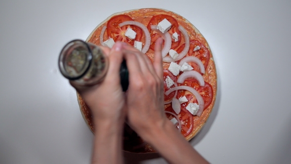 Woman's Hands Sprinkling Spices From Mill On Greek Pizza With Feta Cheese