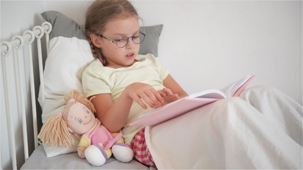 Little Girl With Glasses Leafing Through a Book While Lying In Bed. Perhaps a Child Is Sick alt
