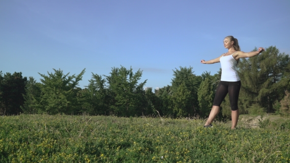 The Girl In a White T-shirt Makes The Wheel Back And Forth On a Hill With Grass. alt