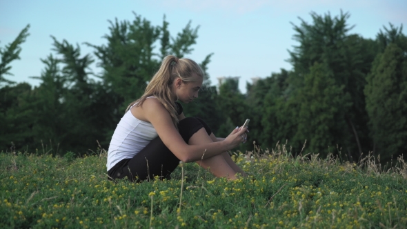Young Girl Shirt Sits On a Hill And Gaining a Message On Your Mobile Phone. alt