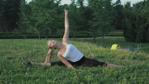 Young Slender Blonde In Shirt Performs Exercise Incline On The Hill With Green Grass In The Park. alt