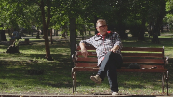 An Old Man Reads a Newspaper On a Bench In The Park. alt
