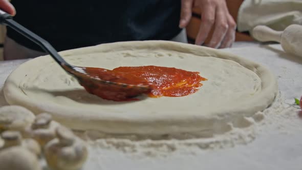 Chef is Spreading Tomato Sauce on Pizza Dough