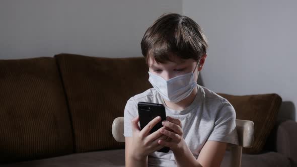 Little Boy in Protective Mask Using Smartphone during the COVID-19 Pandemic