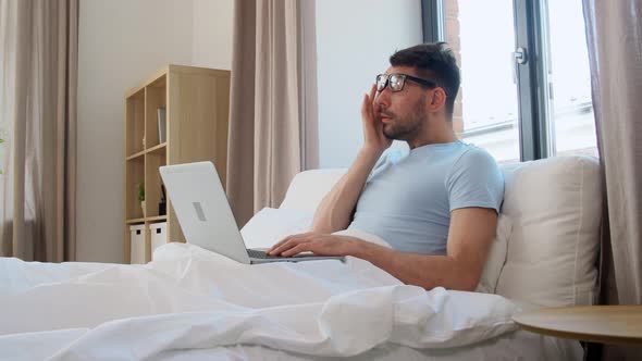 Tired Man in Glasses with Laptop Working in Bed alt