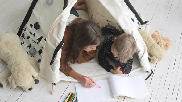 Mother and Son Painting Pencils in Album Together Lying in Tepee in Nursery alt