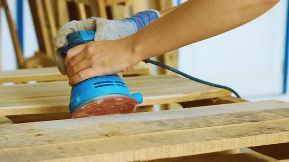A Young Woman Holding Firmly The Grinder While Polishing The Edges Of A Wooden Pallet - Close Up Sho alt
