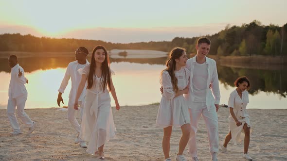 Young People Walk Towards the Camera on the Lake Beach at Sunset