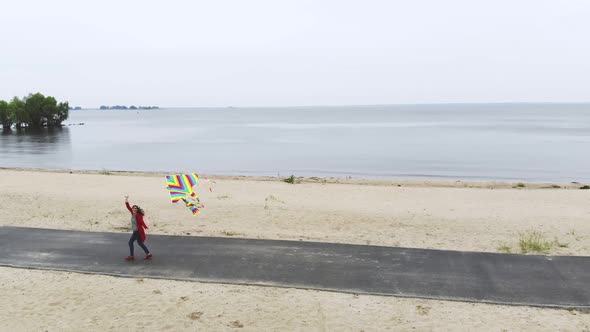 Aero. Woman Flies a Bright, Colorful Rainbow Kite Into the Sky on the Beach. Nice Weather, Spring alt