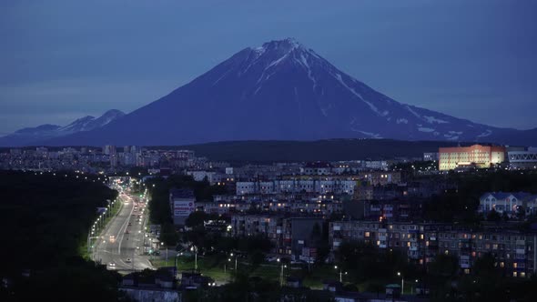 Night Cityscape Driving Cars on City Road on Background of Volcano. Time Lapse