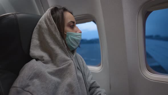 Woman in Hoodie and Medical Mask in Airplane Cabin alt