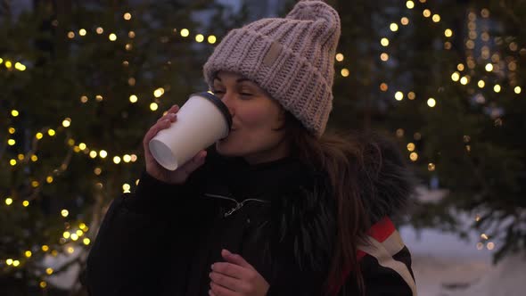 Pretty Young Woman Drinks Hot Coffee Outside at Christmas Market. Cute Girl in Winter, Drinking Hot