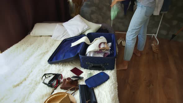A Belated Girl Puts Clothes Together with Hangers in a Suitcase Standing on the Bed with Accessories alt