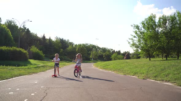 Front View Two Girls Riding Scooter And Bike On Driveway alt