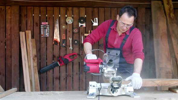 Male Joiner Processes Wood Bar Using a Miter Saw in a Workshop. alt