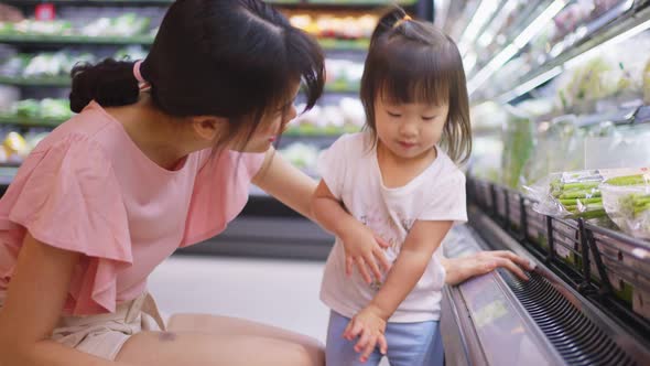 Asian young beautiful mother choosing grocery foods with little kid child walking in supermarket. alt