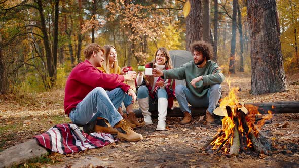 Friends Laughing Cheering with Cups Sitting on Log in Autumn Forest alt