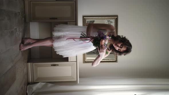 The Girl Stands with Flowers and Looks Into the Camera alt