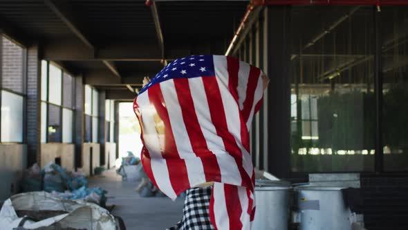 Mixed race woman holding us flag running through an empty building alt