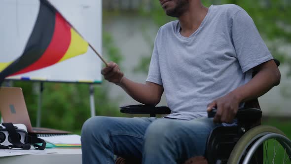 Unrecognizable Paraplegic Man in Wheelchair Fluttering German Flag in Hand Sitting Outdoors on alt