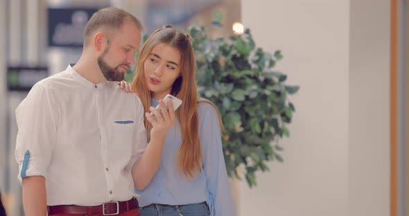 Man and a Woman in a Mall are Looking at a Phone and Talking About Something alt