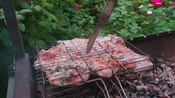 Checking the readiness of the chicken with knife over the burning coals in the grill. alt