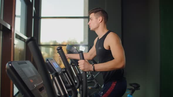 Back View a Man in the Cardio Area of the Gym Trains on an Elliptical Trainer alt