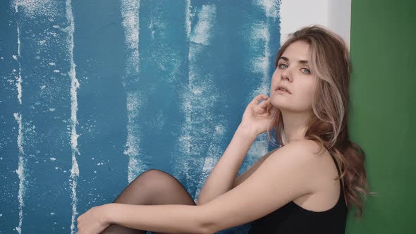 Blonde Sad Woman Wearing a Bodysuit Sits in Green and Blue Studio