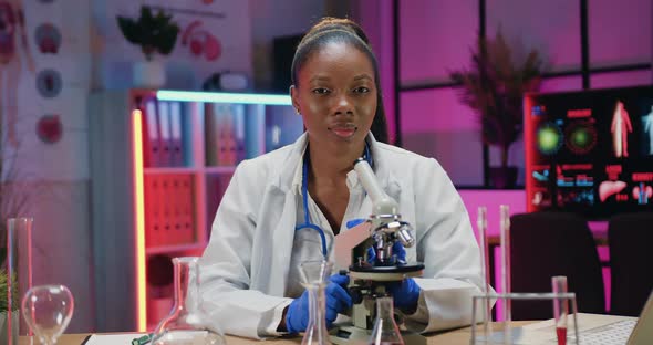 Female Researcher in white Coat Posing on Camera at Her Workplace in Medical Laboratory alt