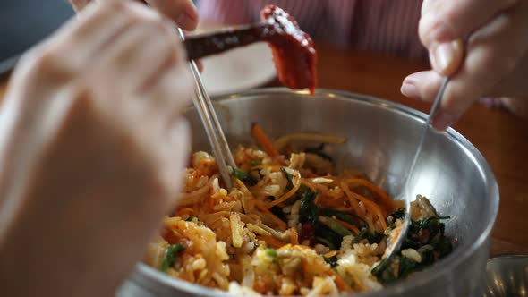 Mixing bibimbap Korean rice and assorted vegetable food dish using stainless spoon