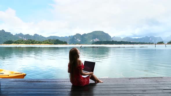 Travel Woman Sitting on Wooden Pier with Laptop Relaxing and Enjoying Nature alt