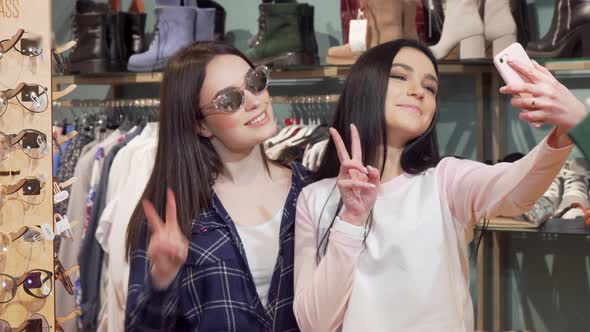 Cheerful Female Friends Taking Selfies with Smart Phone at Clothing Store alt