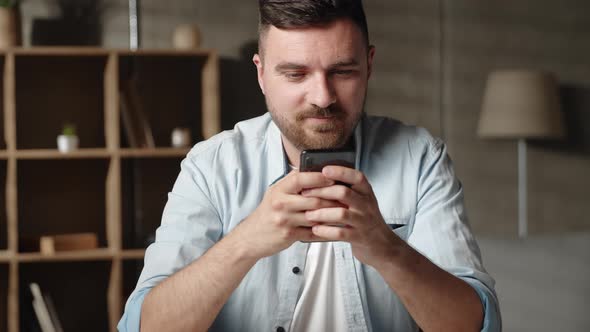 Happy Young 30s Man Looking at Smartphone Screen Reading Message with Pleasant News Enjoying alt
