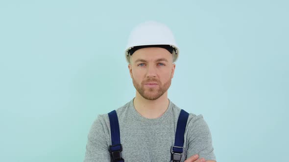 Serviceman in a Helmett and Overalls Looking at Camera on Blue Background alt