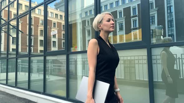 A Business Girl Walks Along a Glass Wall with a Laptop