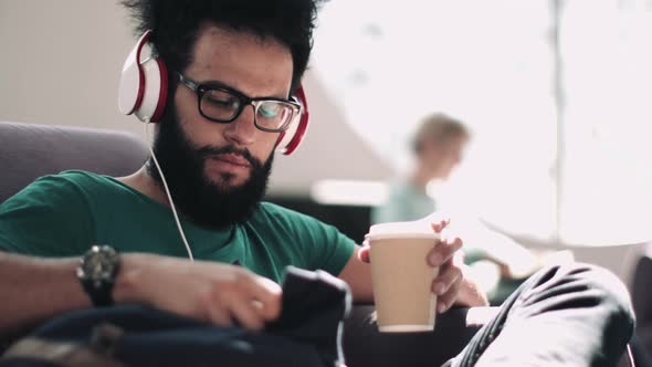 Adult Latin Male in waiting room with coffee cup listening to music on headphones