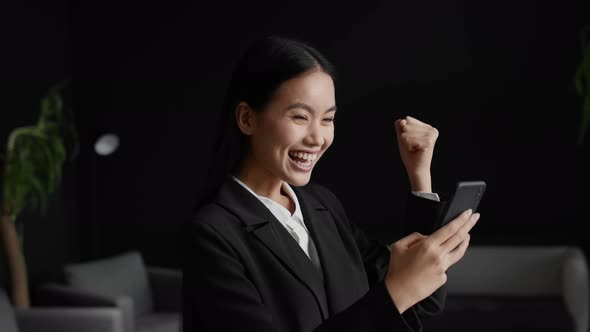Asian Businesswoman Using Phone Gesturing Yes Celebrating Success In Office alt