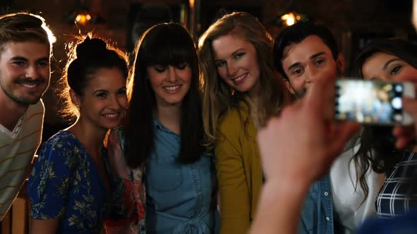 Woman clicking photo of friends on mobile phone alt