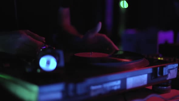 Video clip of dj playing vinyl record on turntables in night club in neon lights alt