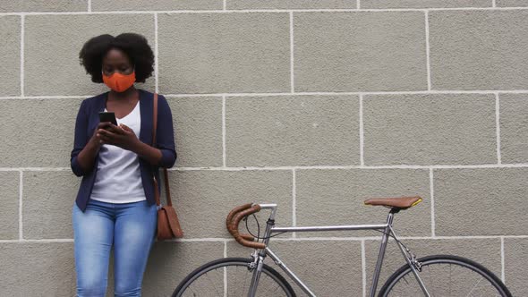 African american woman wearing face mask using smartphone in street alt