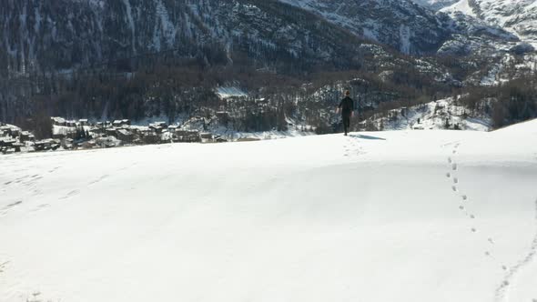 Person walking over snow covered mountain edge and looking over valley alt