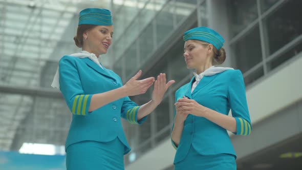Excited Beautiful Stewardess Explaining Work of New Technical Device To Young Colleague in Airport alt