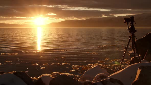 Camera at the edge of a lake during sunset reflecting in winter alt
