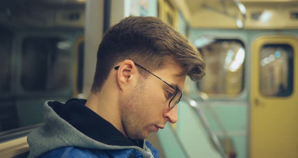 Young Guy with Glasses Rides in an Empty Transport and Carefully Looks alt
