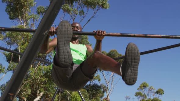 Fit african american man exercising outside, doing hanging pull ups on a climbing frame alt